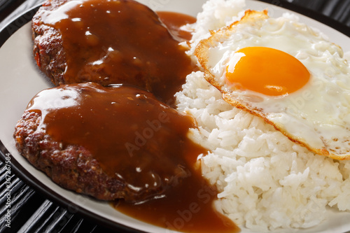 classic Hawaiian dish, Loco Moco consists of steamed rice with juicy hamburger steak, fried egg and gravy close-up on a plate. Horizontal