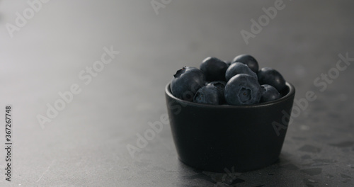 small black bowl with fresh blueberries on concrete surface with copy space