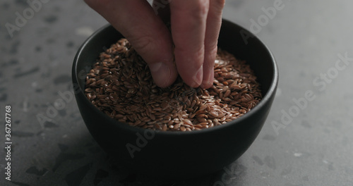 closeup of man hand takes flaxseed from black bowl