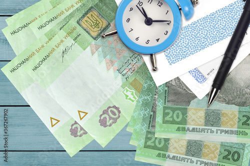 20 Ukrainian hryvnias bills and alarm clock with pen and envelopes. Tax season concept, payment deadline for credit or loan. Financial operations using postal service photo