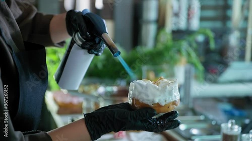 sweets, process of making donuts made by chef by pastry chef, baker burns protein cream on donut with gas burner in kitchen of bakery or cafe photo