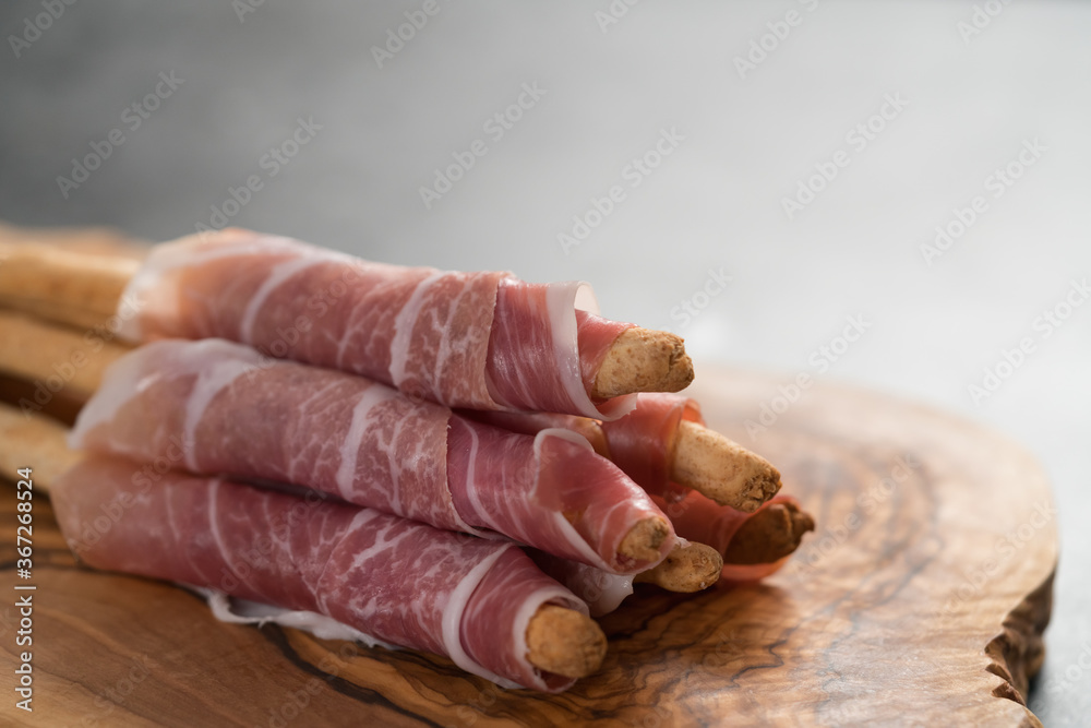 Grissini with prosciutto on olive wood board with copy space