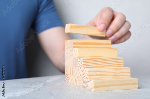Man building steps with wooden blocks on light grey marble table, closeup. Career ladder