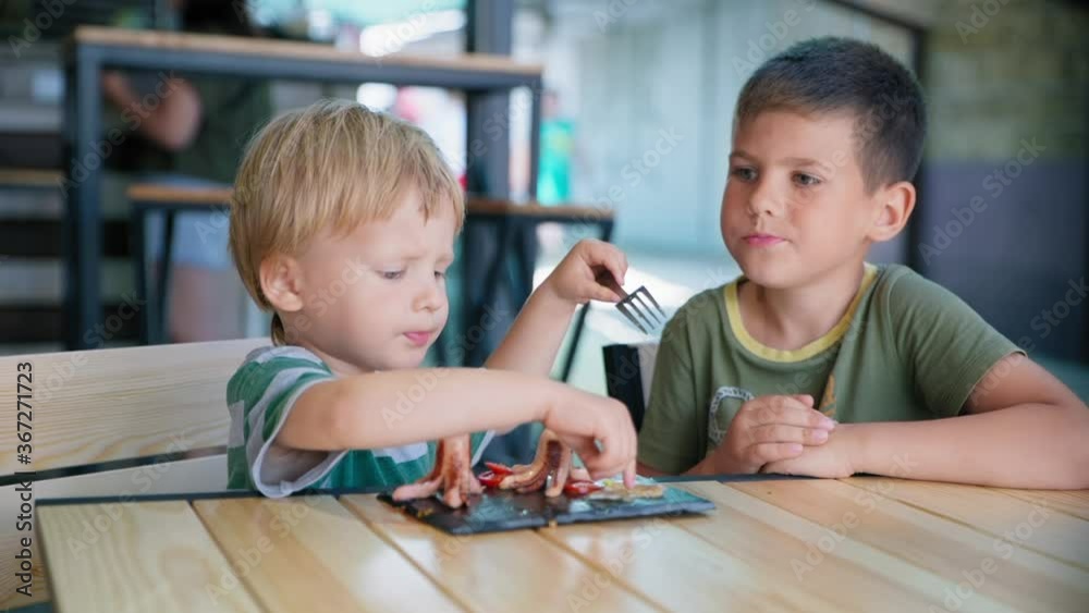 kids food, cute little hungry male child with an appetite eating healthy breakfast grilled sausages and eggs with vegetables in cafe or restaurant