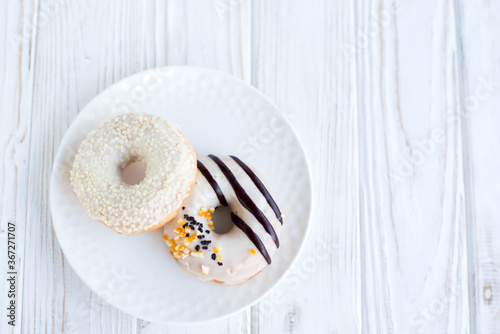 Top view of two donuts on a small white plate with white background. Fresh sweet colorful homemade vanilla donuts on vintage background for birthday or party, with free space for text