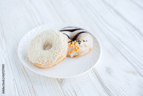 Top view of two donuts on a small white plate with white background. Fresh sweet colorful homemade vanilla donuts on vintage background for birthday or party, with free space for text