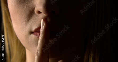 Woman putting finger on mouth. She is showing hush silence sign.