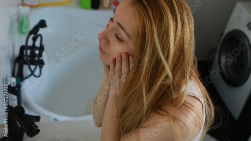 Beautiful young woman is touching her face while looking at the mirror