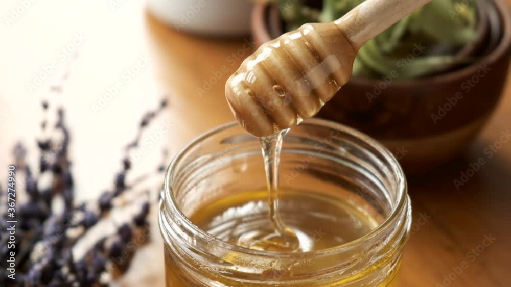 Liquid flower honey in a jar. Honey dripping down from a wooden honey dipper. Natural organic honey Liquid flower honey in a jar. Honey dripping down from a wooden honey dipper. Natural organic honey