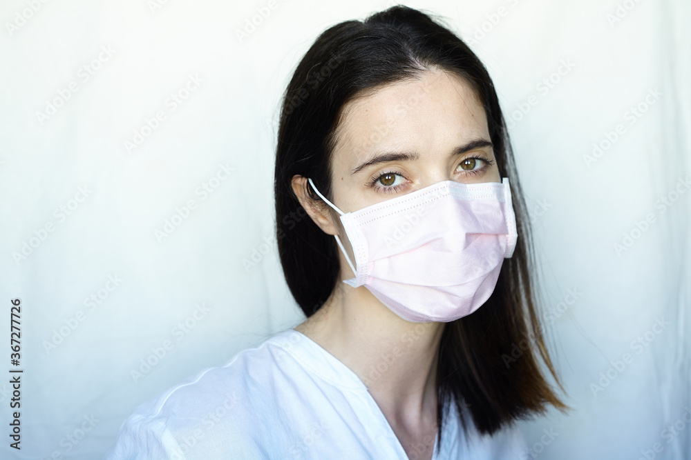 A woman in gloves and a protective mask stands on a light background in a white jacket. The concept of suppression of coronavirus A woman in gloves and a protective mask stands on a light background in a white jacket. The concept of suppression of coronavirus