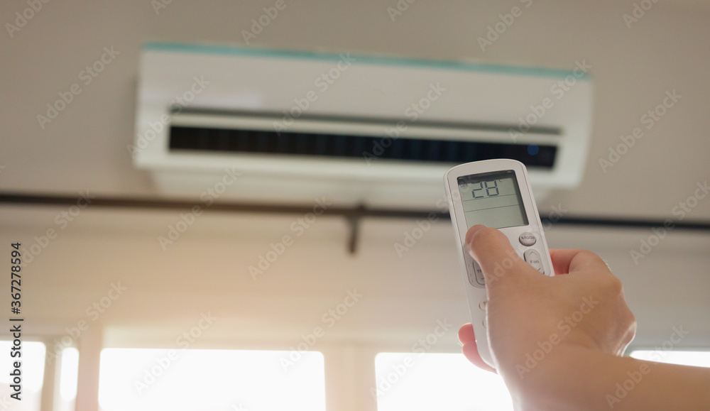 Hand with remote control directed on air conditioner inside the room Hand with remote control directed on air conditioner inside the room