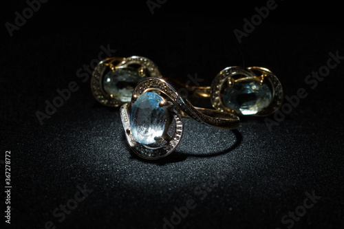 Gold ring with blue diamond and earrings on black background
