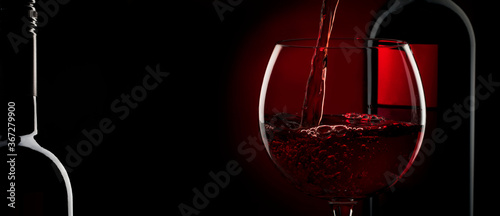 Pouring red wine into the glass against red black background. Panoramic banner with copy space