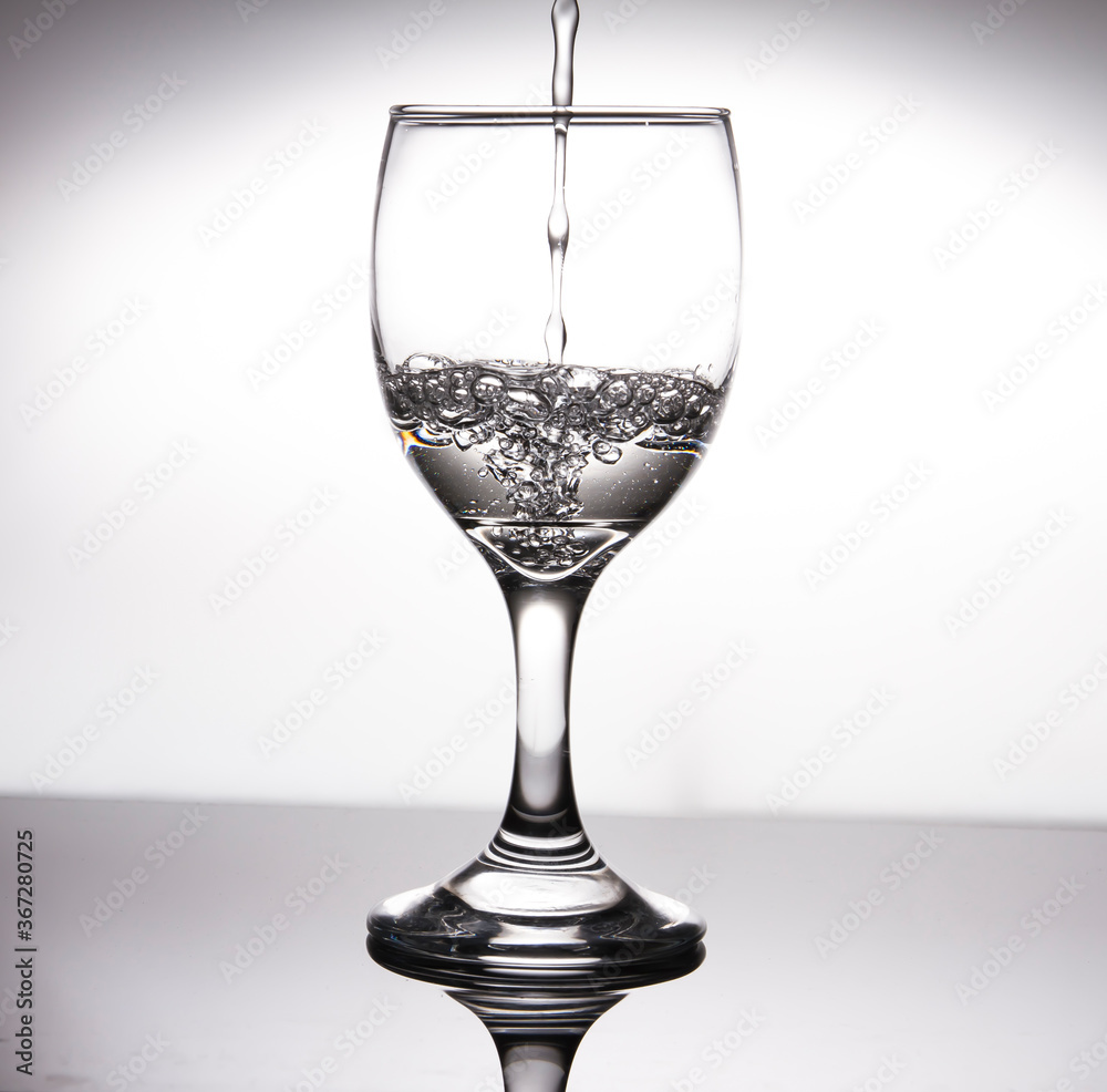 Pour water into half a glass of wine, creating bubbles on a gray background. Pour water into half a glass of wine, creating bubbles on a gray background.