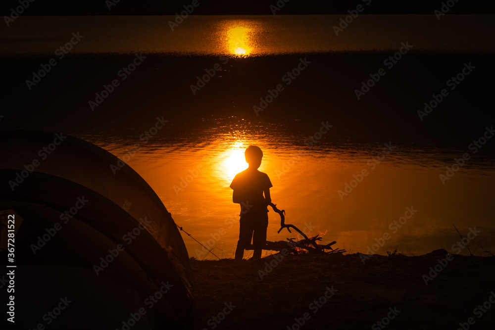 Boy tending to the campfire at sunset in campsite by Shakani lake in Akagera National Park, Rwanda
