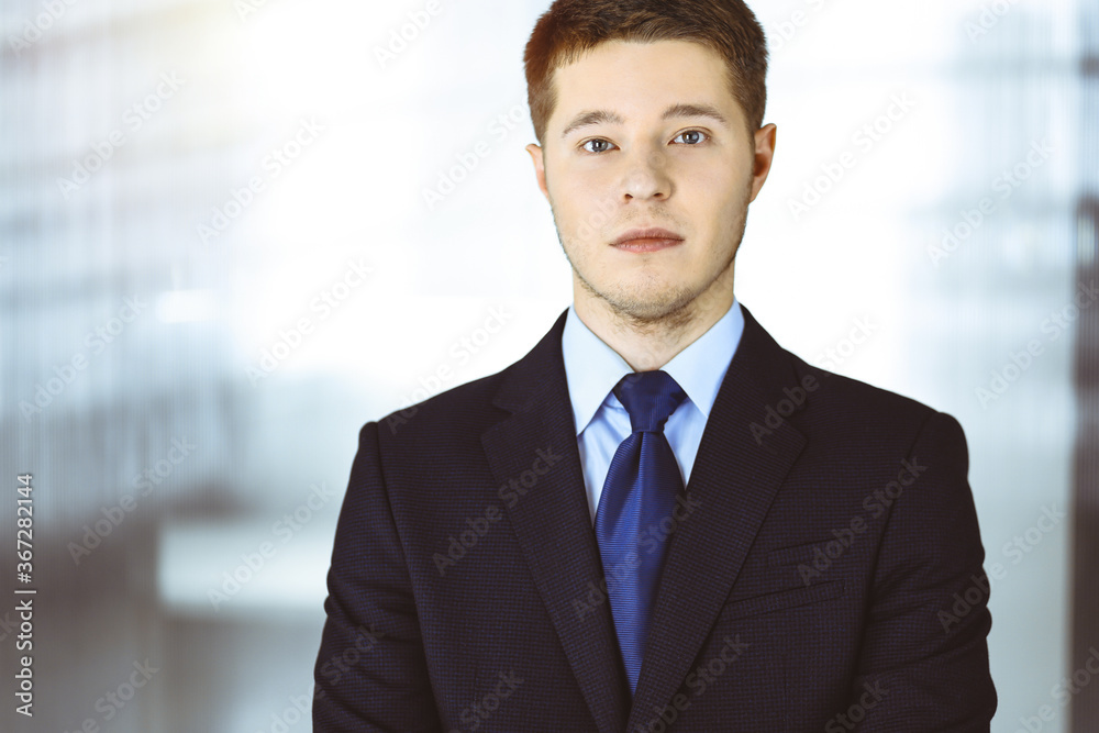 Young businessman in a suit, while standing in a sunny office. Business success concept nowadays Young businessman in a suit, while standing in a sunny office. Business success concept nowadays