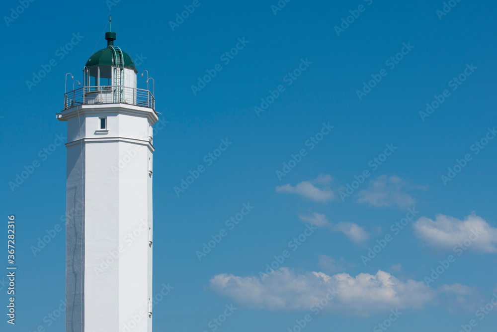 White lighthouse on a background of blue sky. White clouds float across the sky.