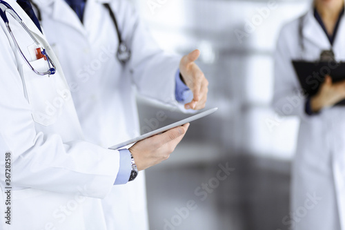 Group of doctors are checking medical names on the computer tablet, when a nurse with a clipboard is making some notes, while standing together in a hospital office. Physicians ready to examine and