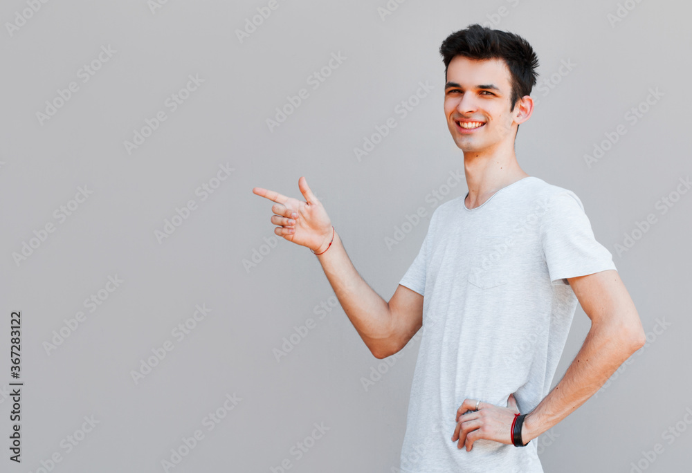 Casual dressed young man in grey t-shirt pointing left with his finger isolated on gray background Casual dressed young man in grey t-shirt pointing left with his finger isolated on gray background