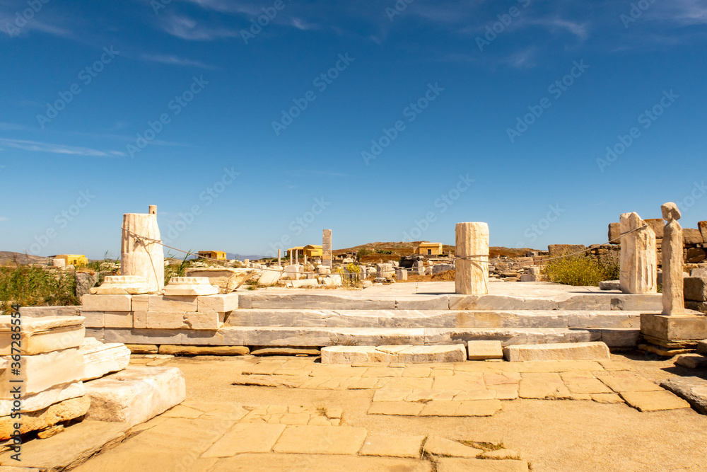 Ruins of an ancient city with stones, columns and temples on DELOS Island - mythological, historical, and archaeological site in Greece with blue sky background.