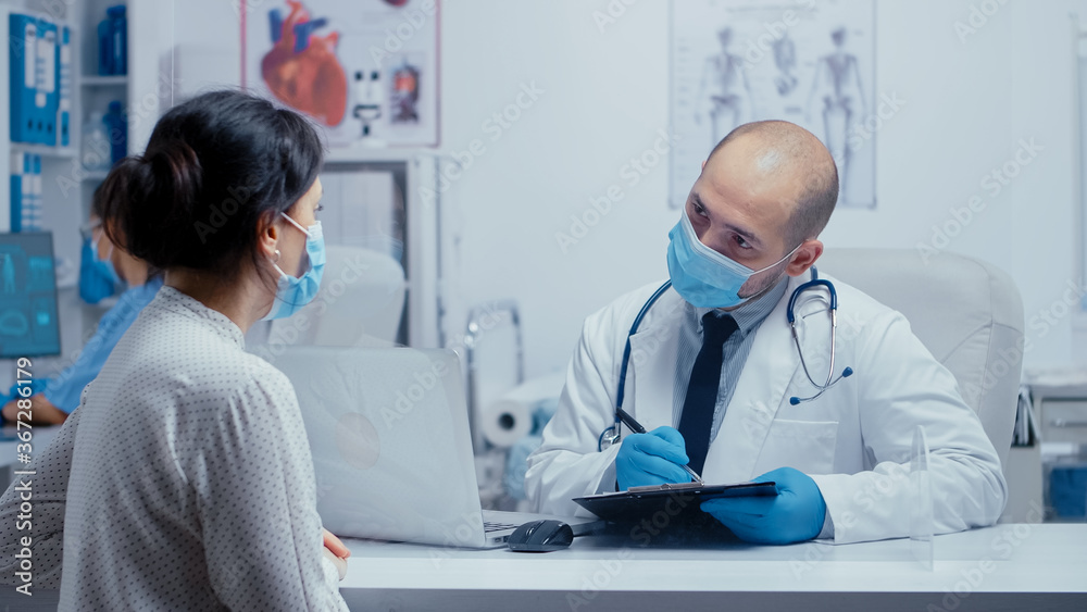 Doctor questioning patient during covid-19 pandemic, writing answears in clipboard. Medical consultation in protective equipment concept shot of sars-cov-2 global health pandemic crisis