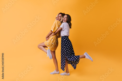 Full-length portrait of fascinating girl in long skirt dancing with friend. Glad female models in stylish clothes expressing happiness.