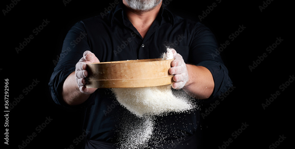 Φωτογραφία chef a man in a black uniform holds a round wooden sieve in his hands and sifts
