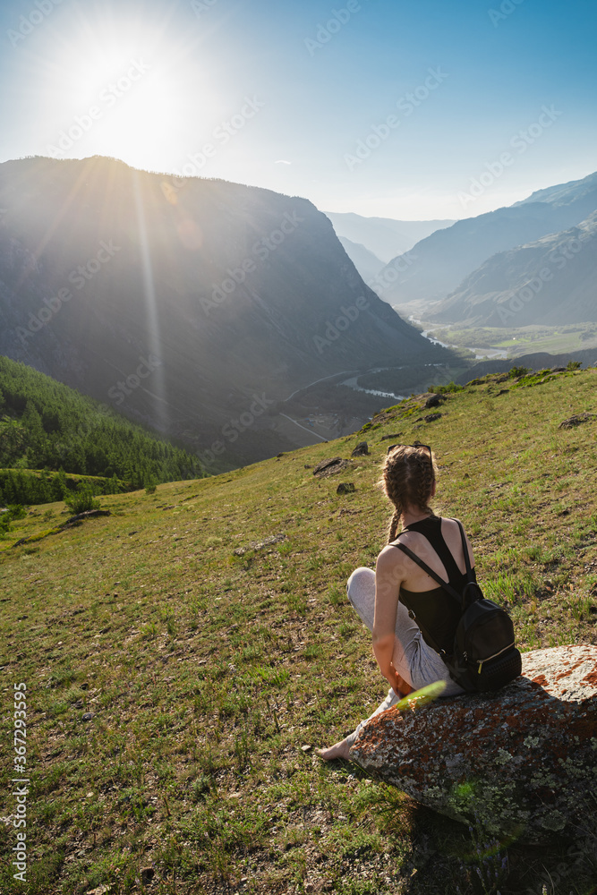 Young woman sits on the top against the background of a beautiful valley between the mountains. Backpack hiking.
