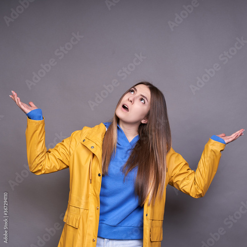 A young white lady in a yellow raincoat raised her hands up, soon it will rain.
