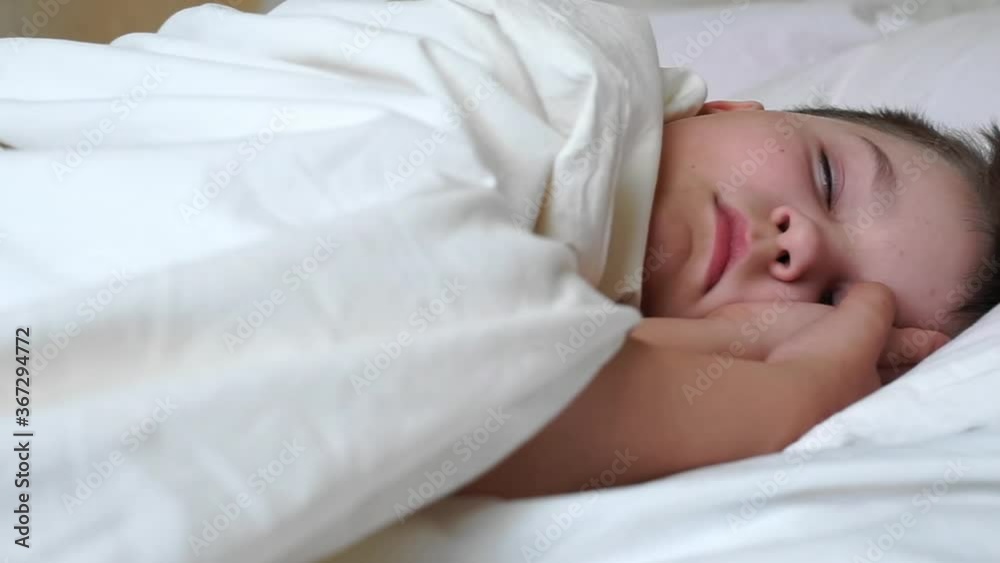caucasian child boy sleeping in white bed lying on soft pillow. caucasian young baby kid resting covered with blanket on white sheets in bedroom in morning. dreamy kid sleep with closed eyes caucasian child boy sleeping in white bed lying on soft pillow. caucasian young baby kid resting covered with blanket on white sheets in bedroom in morning. dreamy kid sleep with closed eyes
