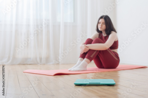 sad teenager girl on floor with scales