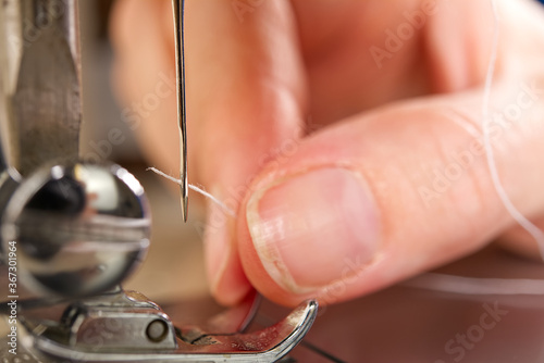 woman threading a needle on a sewing machine. close up, selective focus.