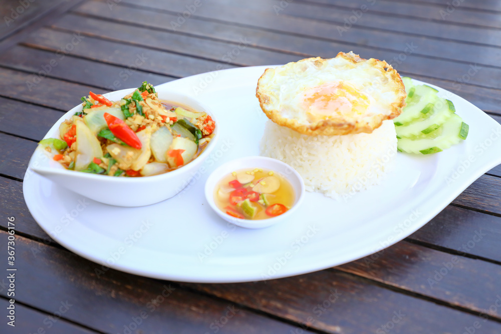 Pad Ka-prao; stir fried chopped chicken with chili and basil, served with steamed rice and fried egg on top set on wooden table Pad Ka-prao; stir fried chopped chicken with chili and basil, served with steamed rice and fried egg on top set on wooden table