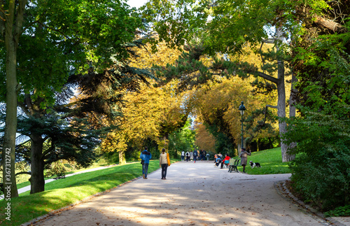 People enjoying tree-lined alley-ways of the Buttes-Chaumont park in Paris, France