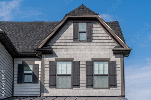 Gable with light shake shingle siding facade, double hung window, dark brown frame, on a Dutch pitched roof attic, American luxury single family colonial home neighborhood in USA blue sky, Alps style