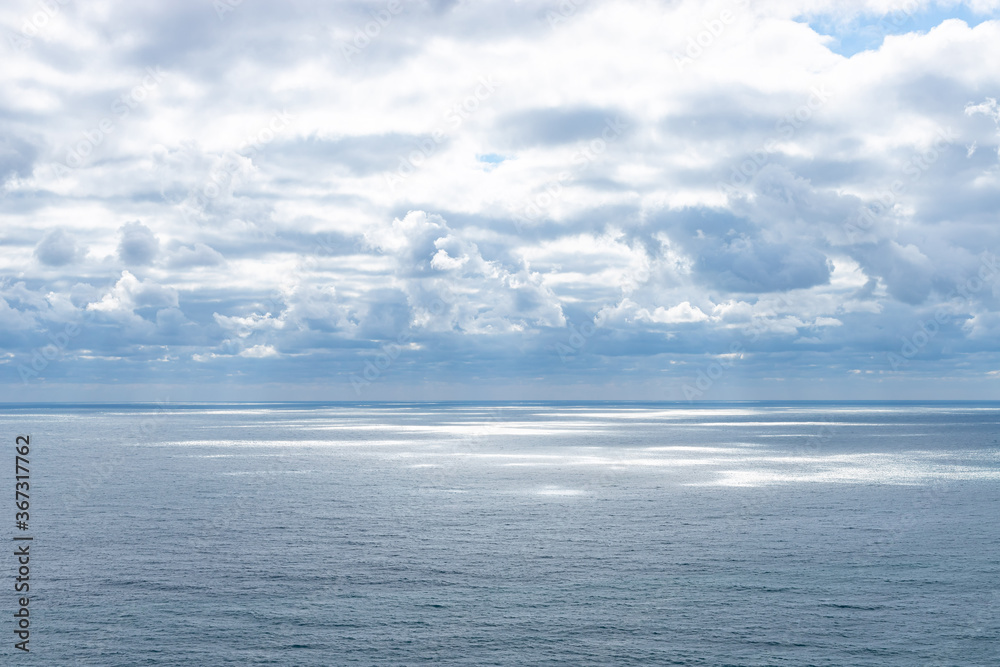 Beautiful clouds on blue sky over calm sea with sunlight reflection. Seascape