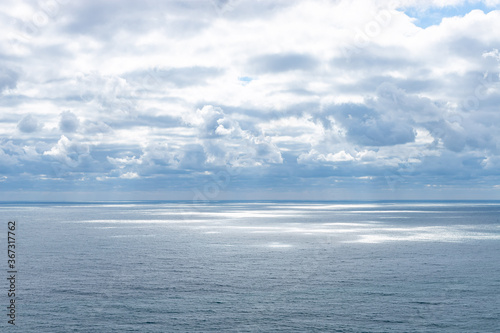 Beautiful clouds on blue sky over calm sea with sunlight reflection. Seascape