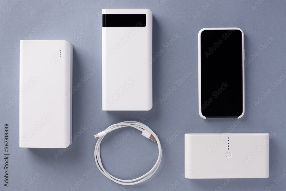 three various Power bank chargers of different capacities, USB cable and smartphone on a blue background. Modern digital concept. top view. three various Power bank chargers of different capacities, USB cable and smartphone on a blue background. Modern digital concept. top view.