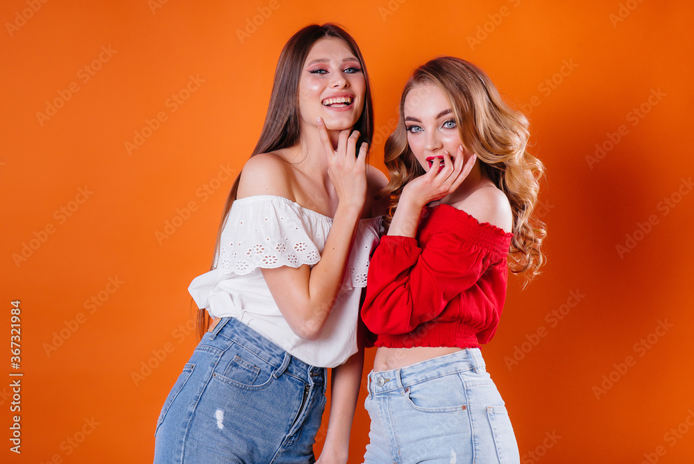 Two young and beautiful girls shows emotions and smiles in the Studio on an orange background. Girls for advertising Two young and beautiful girls shows emotions and smiles in the Studio on an orange background. Girls for advertising