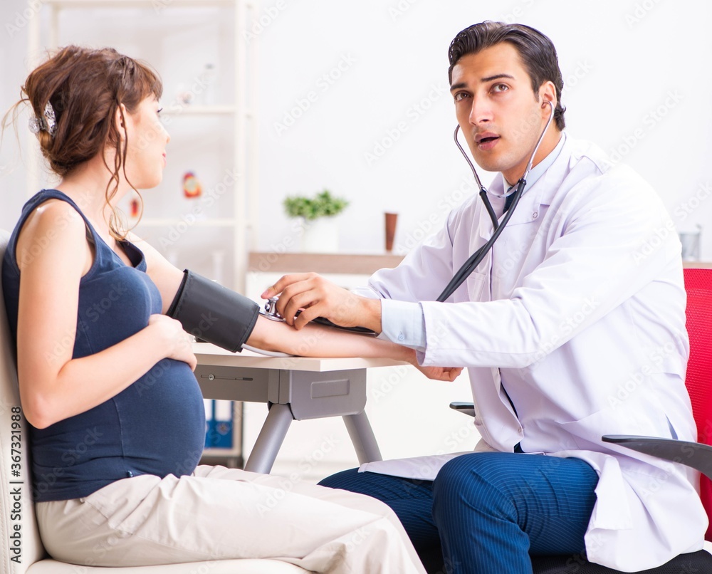 Young doctor checking pregnant woman's blood pressure - obrazy, fototapety, plakaty 
