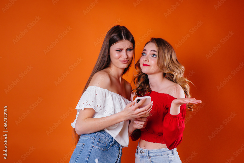 Two young and beautiful girls take a selfie and watch the phone in the Studio on a purple background. Girls for advertising Two young and beautiful girls take a selfie and watch the phone in the Studio on a purple background. Girls for advertising