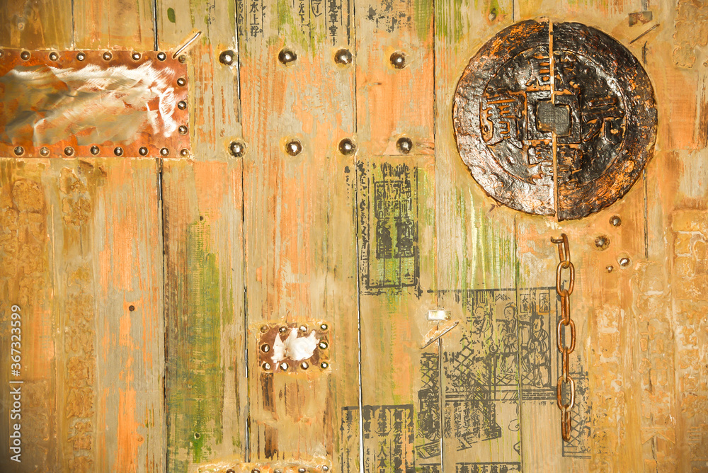 Part of wooden door with chinese signs and metal ornaments and chain.