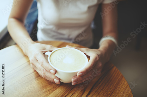 Female hands holding cup of coffee in cafe. Blurred image, selective focus
