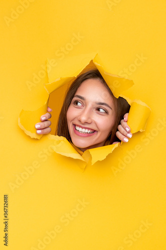 Happy young woman peeping out of hole in paper © kegfire