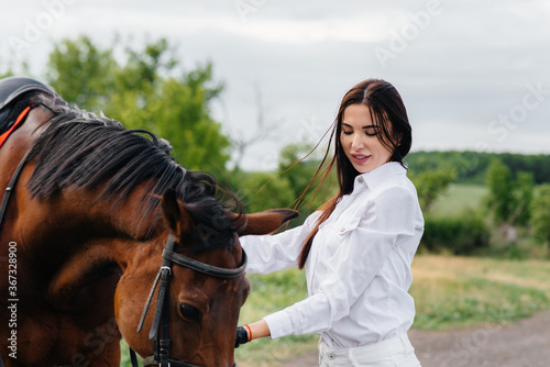 A young pretty girl rider poses near a thoroughbred stallion on a ranch. Horse riding, horse racing