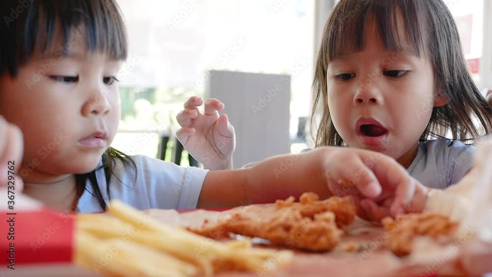 Happy Asian sibling sisters enjoy with eating fried chicken and French fries in service shop. Junk food and Health concepts. Happy Asian sibling sisters enjoy with eating fried chicken and French fries in service shop. Junk food and Health concepts.