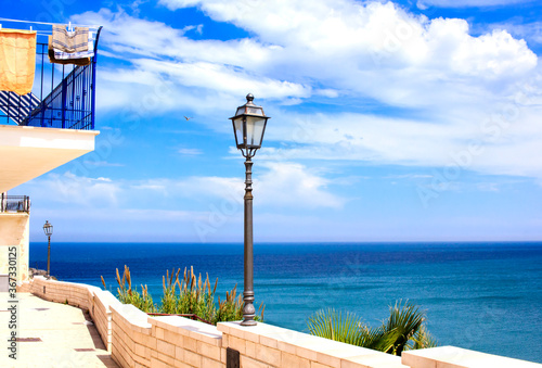 Promenade by the seaside in Vieste town, Puglia, Italy. Picture features horizon over sea with beautiful cloudscape and some city installations on the foreground : lamppost, stone fence, balcony.