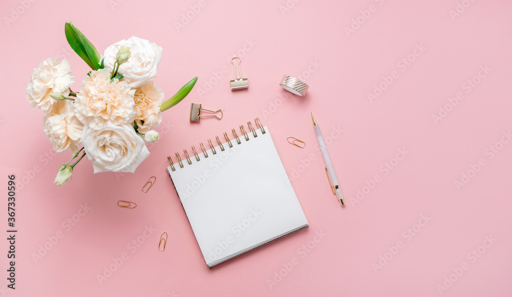 Stationery business flatlay creative composition. Top horizontal view of envelope, spiral blocj paper clips and a pen on abstract pink background.