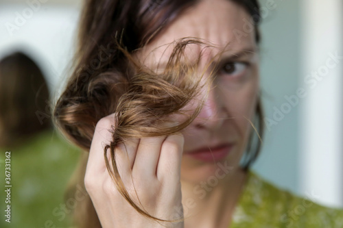 Woman looking at her dry and tangled hair ends. 