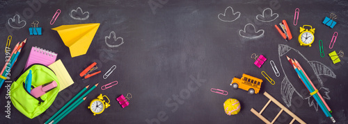 Back to school background with bag backpack, rocket sketch and school supplies over chalkboard. Top view from above